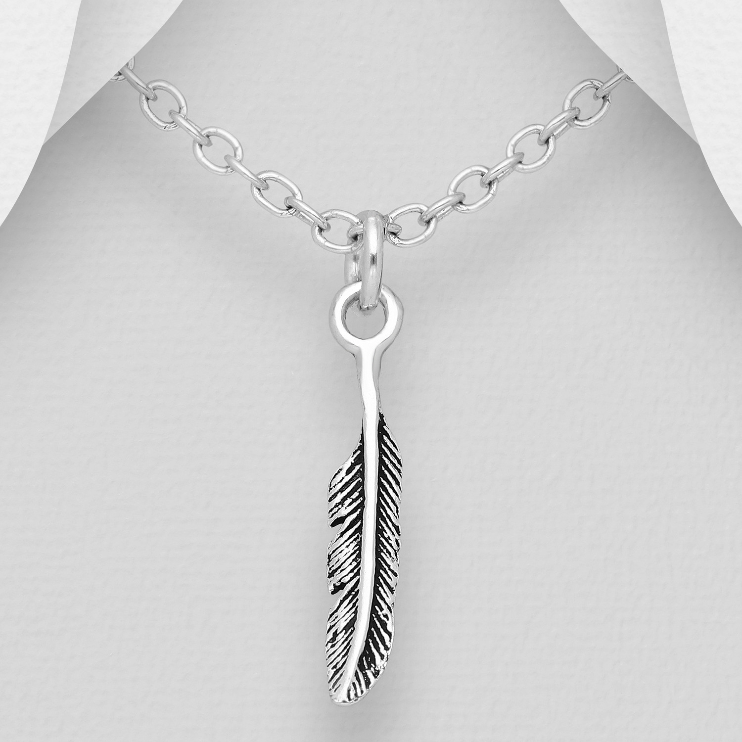 Small sterling silver oxidised feather pendant shown on a chain against a grey background
